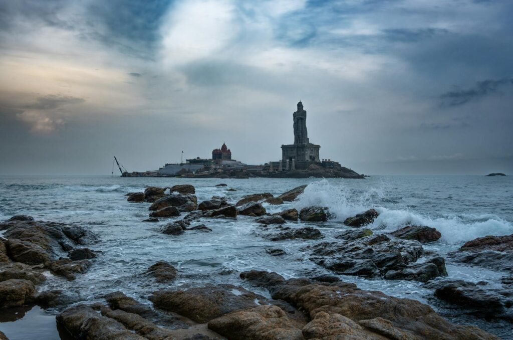 Stunning view of Thiruvalluvar Statue and ocean waves in Kanniyakumari during sunset.